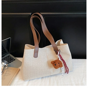 Detail of off-white canvas tote bag with brown leather straps and plush bear charm