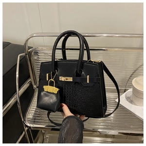 Detail of luxury black handbag with crocodile texture, gold clasp and mini charm pouch