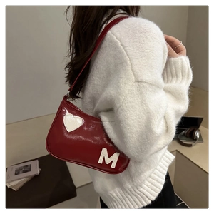 Detail of red patent leather underarm bag with white heart and M patch on a white sweater