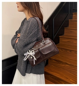 Détail du sac à bandoulière marron brillant avec poches avant et pendentif en dentelle