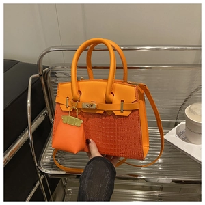 Detailed view of crocodile texture on orange handbag with metallic lock and mini charm