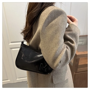 Detailed view of black patent leather shoulder bag with embossed M on wool coat