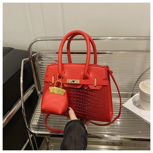 Detail of red croc-texture handbag featuring gold twist lock and mini bag charm accessory