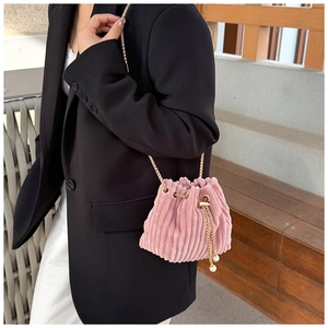Pink corduroy drawstring bucket bag with gold chain strap and pearl accents on model