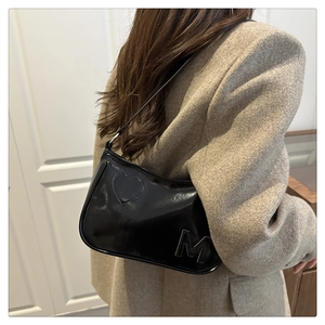 Detail showing shiny black patent leather surface with heart patch and letter M on shoulder bag