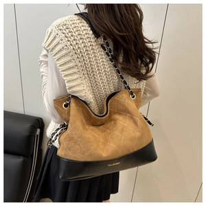 Close-up of quilted suede tote bag with metal chain strap and brand lettering detail