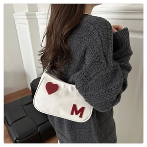 Close-up of white glossy shoulder bag featuring a red heart and M letter patch on model