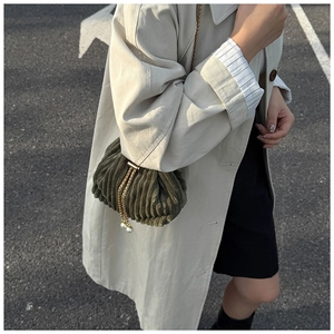 Close-up of dark green corduroy bucket bag with gold chain and pearl details