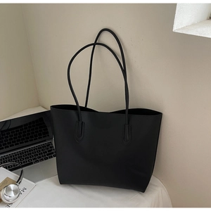 Minimalist black tote bag with long shoulder straps next to a laptop and headphones
