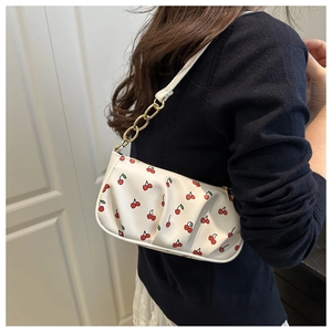 Detail of ruched white underarm bag with red cherry print and gold chain strap