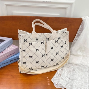 Large beige corduroy tote bag with black bow print and twin front pockets on a wooden bench