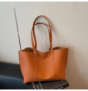 Detail of orange tote bag with decorative buckle strap and long handles on a book
