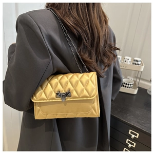 Detail of ginger yellow quilted square bag with rhombic stitching and metal chain