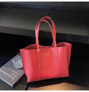 Detail of red matte leather tote bag with gold lettering on elegant dark background