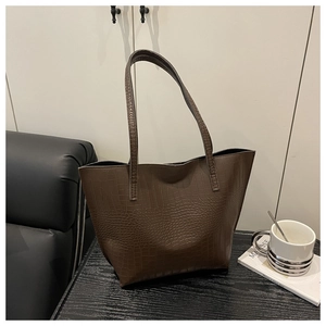 Detail of deep brown crocodile pattern tote bag with dual slim straps on leather sofa
