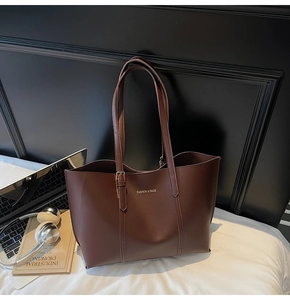 Close-up of brown leather tote bag with metal buckle and gold fashion lettering logo