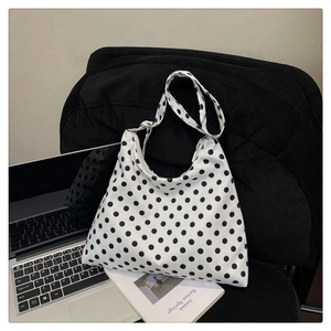 Polka dot nylon tote bag with wide shoulder strap placed on a chair with a laptop