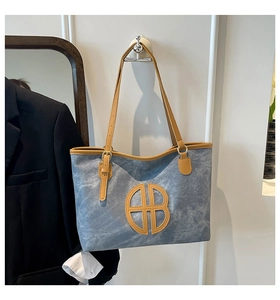Detail of blue textured tote bag featuring brown leather trim and metallic buckle