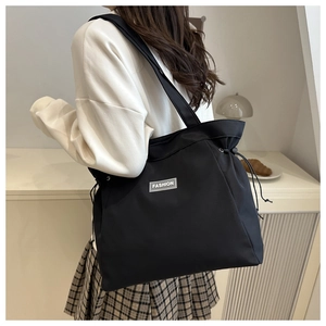 Detail of black nylon tote bag with drawstring closure and Fashion label on shoulder