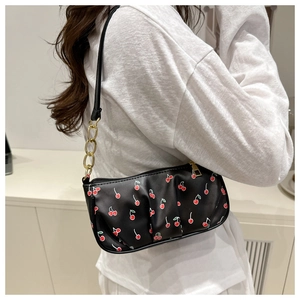 Detail of cherry print shoulder bag featuring black faux leather and gold chain strap