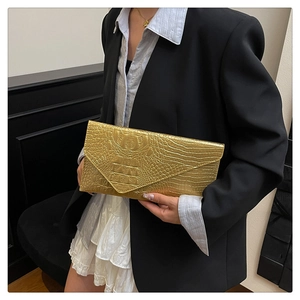 Dettaglio di una pochette a busta dorata con stampa coccodrillo tenuta da una modella