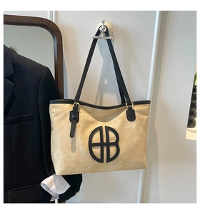 Detailed view of beige suede tote bag with black circular logo and adjustable strap
