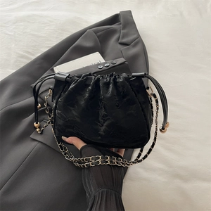 Elegante borsa a secchiello nera a pieghe con catena oro su blazer grigio