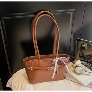Detail of vintage brown shoulder bag with sleek leather texture and plaid bow charm