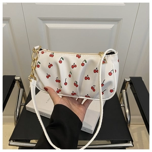 Detail of white baguette bag with cherry print, gold chain and pleated faux leather
