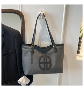 Detail of grey matte tote bag showing golden ring hardware and black leather strap