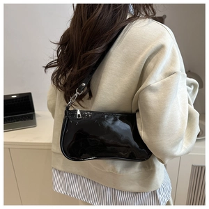 Detail of glossy black patent leather baguette bag with silver hardware on shoulder