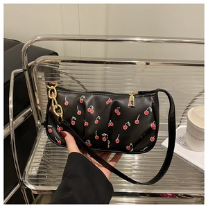 Detail of black baguette bag featuring red cherry print and golden chain handle