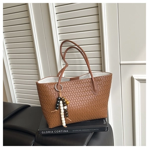 Detail of brown woven leather tote with decorative beaded charm on a leather seat