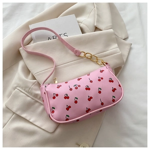 Close-up of pink baguette bag with cherry print and golden chain strap on a blazer