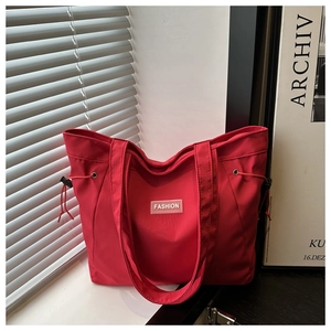 Detail of red nylon tote bag with Fashion label and drawstring cinch on a bright window ledge