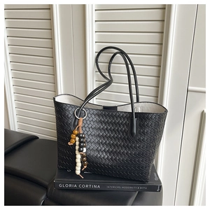 Detailed shot of black woven tote bag featuring decorative wooden bead tassel and slim strap