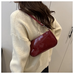 Detail of red glossy patent leather baguette shoulder bag worn by model on shoulder