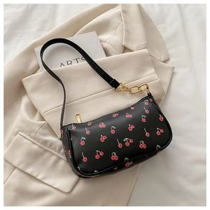 Detail of cherry print shoulder bag with gold chain on beige blazer and art book