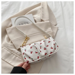 Detail of white baguette bag with red cherry prints and golden chain strap