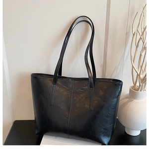 Detail of minimalist black faux leather tote bag showing glossy texture and vertical seam