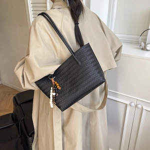 Minimalist black woven leather tote bag with a wooden bead charm on a beige trench coat