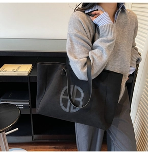 Detail of the black faux suede tote bag featuring a circular logo and slim shoulder strap