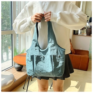 Detail of blue nylon tote bag with pleated fabric and three front utility snap pockets