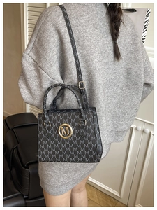 Close-up of crossbody bag featuring 'M' monogram print and gold circular metal logo detail