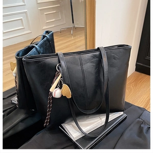 Detailed view of black oil wax leather tote bag featuring a baseball themed charm on strap