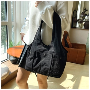 Detail of black pleated tote bag showing three external pockets with metal snap fasteners