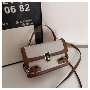 Detail of a vintage-style beige canvas and brown leather crossbody bag with a metal twist lock