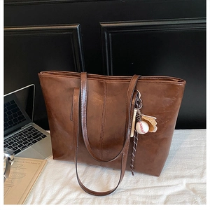 Brown oil wax leather tote bag with baseball pendant in an office setting with laptop