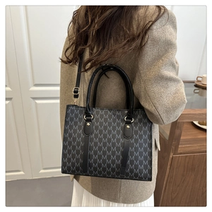 Detail of woman carrying a vintage M-print tote bag with gold metal buckles and top handles