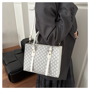 Detail view of white monogram tote bag with gray M pattern worn by a model in gray blazer